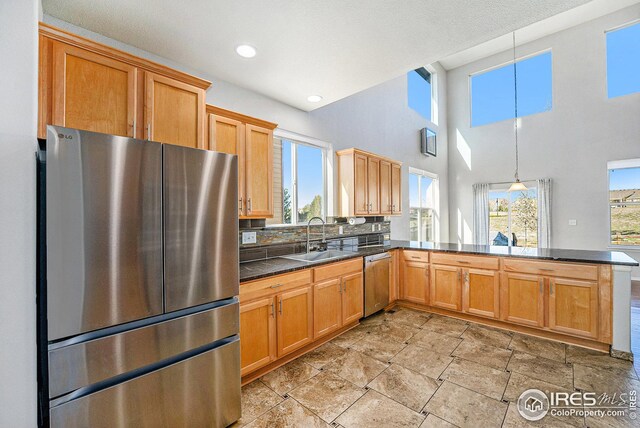 kitchen featuring a sink, a peninsula, tasteful backsplash, dark countertops, and appliances with stainless steel finishes