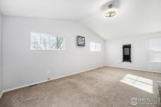 spare room featuring carpet flooring, visible vents, baseboards, and vaulted ceiling