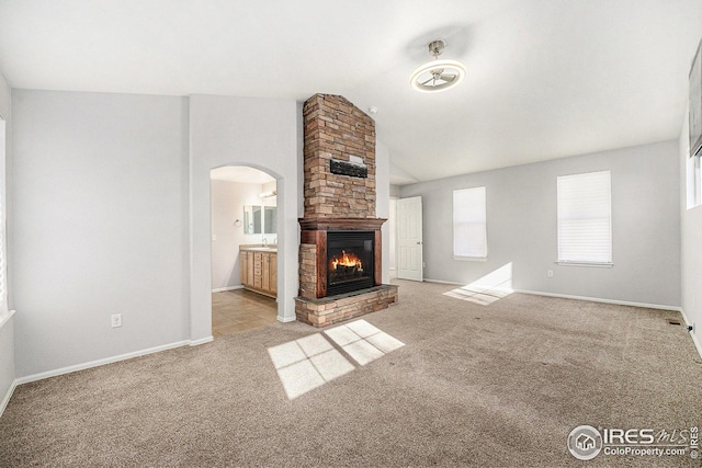unfurnished living room with a large fireplace, carpet flooring, arched walkways, and baseboards