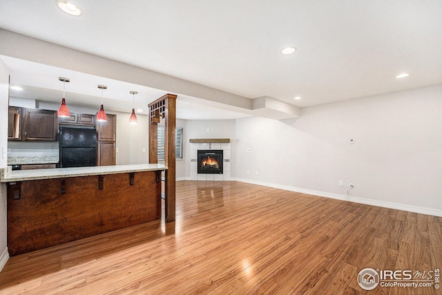 unfurnished living room featuring baseboards, recessed lighting, a tiled fireplace, and light wood-type flooring