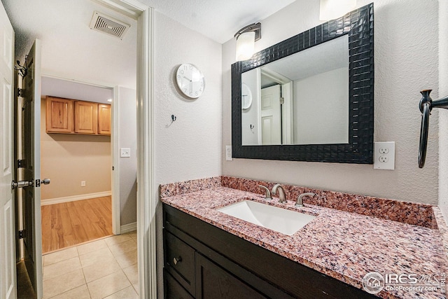 bathroom featuring visible vents, baseboards, tile patterned flooring, a textured wall, and vanity