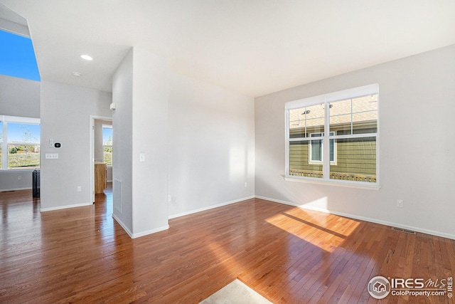 unfurnished room with a wealth of natural light, baseboards, visible vents, and wood finished floors