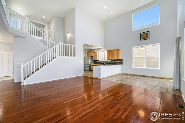 unfurnished living room featuring a towering ceiling, stairs, hardwood / wood-style floors, and visible vents