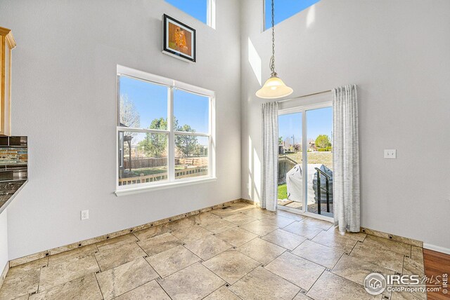 unfurnished dining area featuring baseboards, a towering ceiling, and stone tile flooring