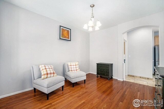 sitting room featuring arched walkways, a notable chandelier, light wood-style floors, and baseboards