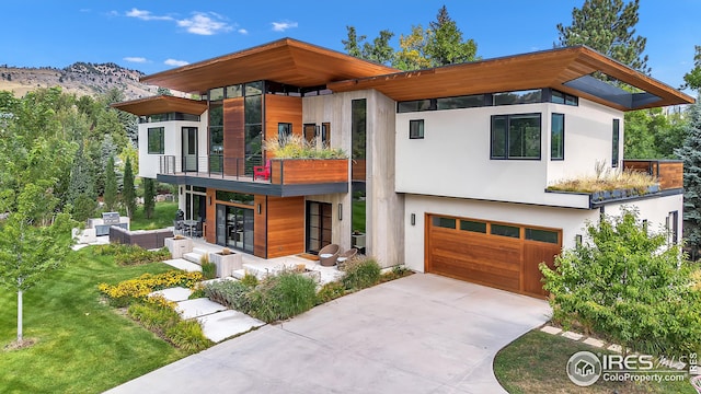 modern home featuring a front yard, an attached garage, concrete driveway, stucco siding, and a balcony