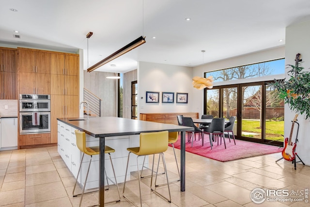 kitchen featuring dark countertops, a sink, a breakfast bar area, double oven, and a center island with sink