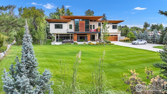 modern home with a front yard, an attached garage, a balcony, stucco siding, and driveway