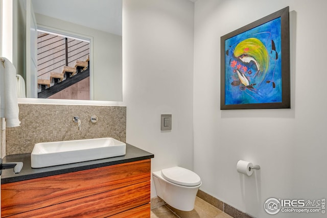 half bathroom featuring tile patterned floors, toilet, baseboards, decorative backsplash, and vanity