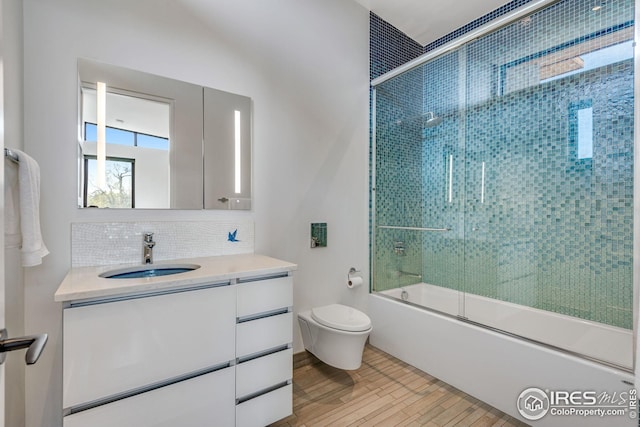 full bath with bath / shower combo with glass door, toilet, vanity, wood finished floors, and backsplash