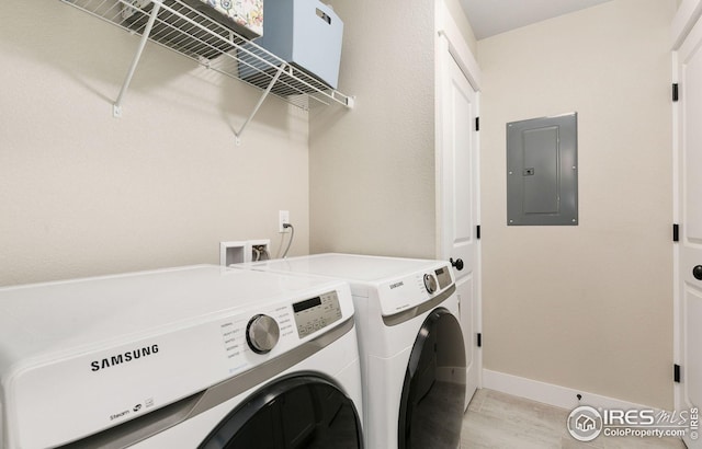laundry area featuring baseboards, electric panel, laundry area, light wood-style floors, and washer and clothes dryer