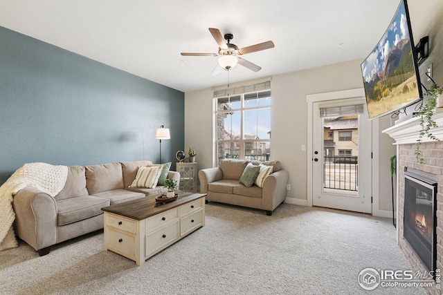 living area with ceiling fan, baseboards, a glass covered fireplace, and light carpet