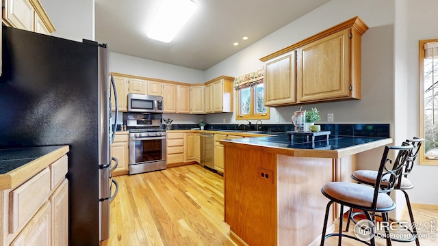 kitchen featuring a peninsula, light brown cabinets, a breakfast bar area, and stainless steel appliances
