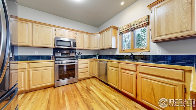 kitchen featuring stainless steel appliances, light wood-style floors, a sink, and light brown cabinetry