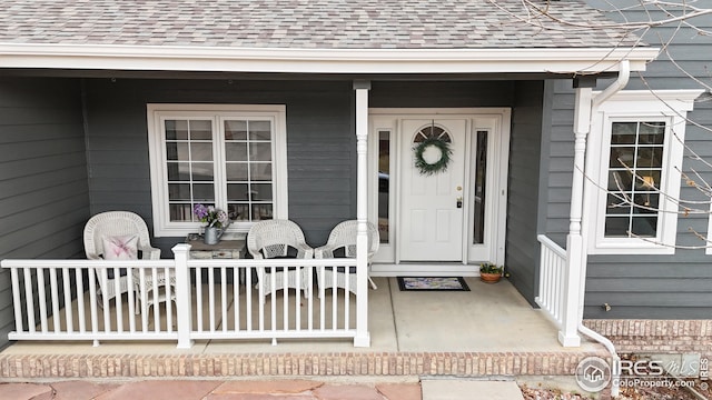 entrance to property featuring a porch and a shingled roof