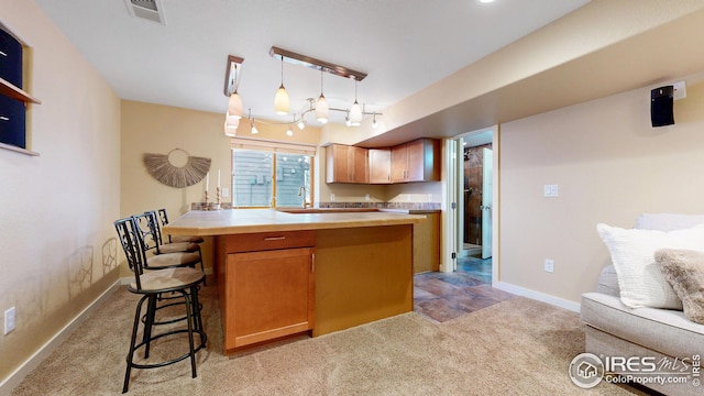 kitchen with a breakfast bar, baseboards, rail lighting, visible vents, and light colored carpet