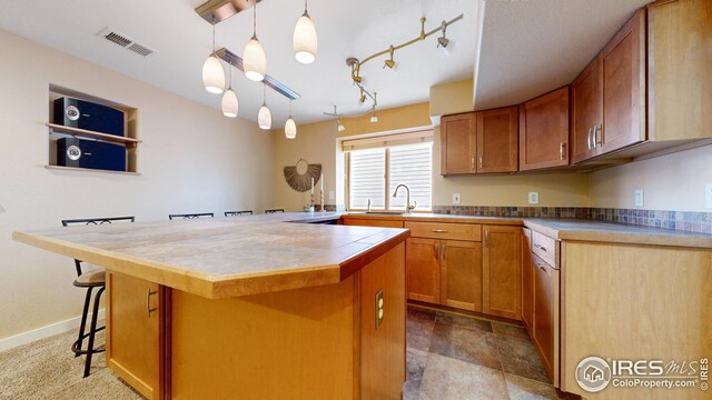 kitchen with a kitchen bar, visible vents, a kitchen island, a sink, and brown cabinets