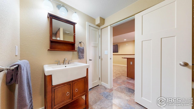 bathroom featuring baseboards, stone finish floor, vanity, and a textured wall