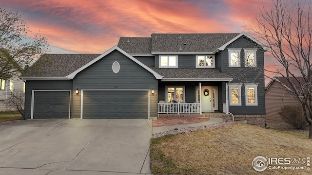 traditional home with roof with shingles, covered porch, a garage, and concrete driveway