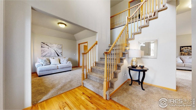 stairs with baseboards, a towering ceiling, carpet, and wood finished floors
