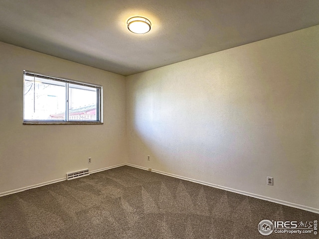unfurnished room with dark carpet, visible vents, and baseboards