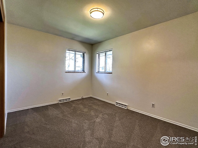 empty room featuring dark colored carpet, visible vents, and baseboards