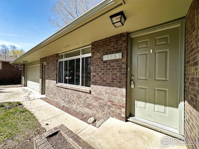 view of exterior entry featuring brick siding, driveway, and an attached garage
