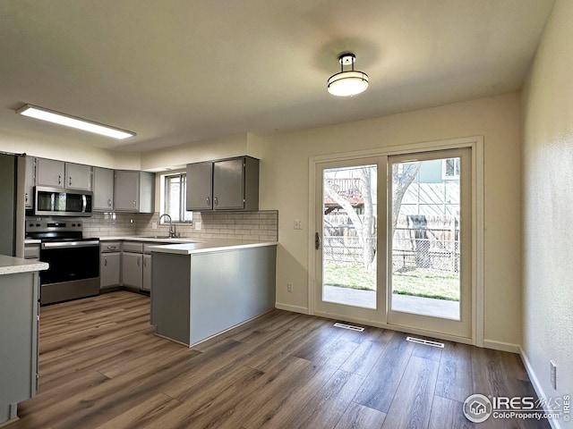 kitchen with stainless steel appliances, gray cabinetry, backsplash, and dark wood finished floors