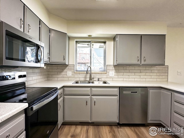 kitchen with gray cabinetry, appliances with stainless steel finishes, wood finished floors, and a sink
