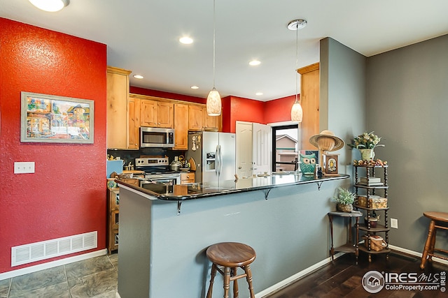 kitchen featuring appliances with stainless steel finishes, dark countertops, a peninsula, a breakfast bar, and baseboards