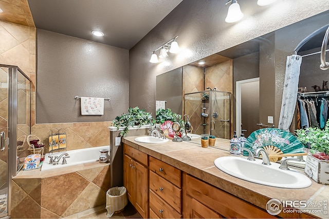 bathroom featuring a textured wall, a shower stall, a bath, double vanity, and a spacious closet