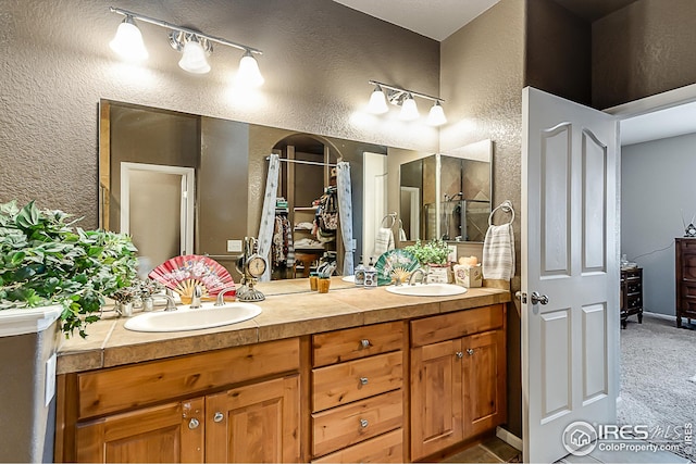 full bathroom featuring a textured wall, double vanity, and a shower