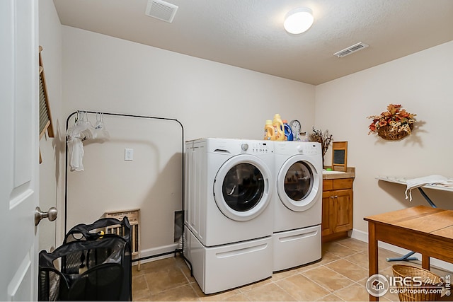 clothes washing area featuring washing machine and dryer, cabinet space, light tile patterned floors, and a textured ceiling
