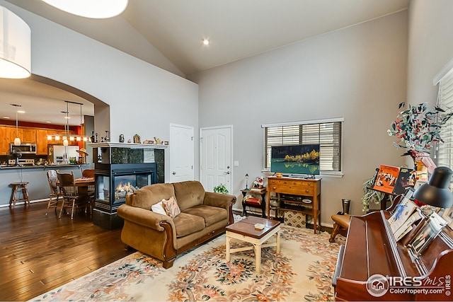 living room featuring high vaulted ceiling, wood-type flooring, a tile fireplace, arched walkways, and recessed lighting