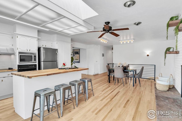kitchen with a kitchen bar, white cabinetry, under cabinet range hood, appliances with stainless steel finishes, and wooden counters