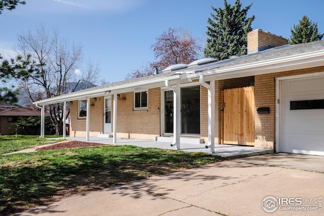 rear view of property featuring a yard, a garage, driveway, and brick siding