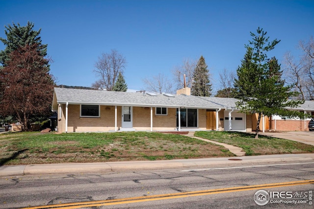 single story home featuring a chimney, driveway, an attached garage, a front yard, and brick siding