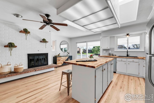 kitchen featuring wood counters, light wood finished floors, a sink, and a brick fireplace