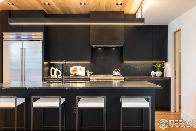 kitchen with stainless steel built in refrigerator, a sink, a kitchen bar, stove, and dark cabinets