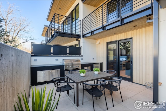 view of patio featuring a balcony, outdoor dining space, grilling area, fence, and an outdoor kitchen