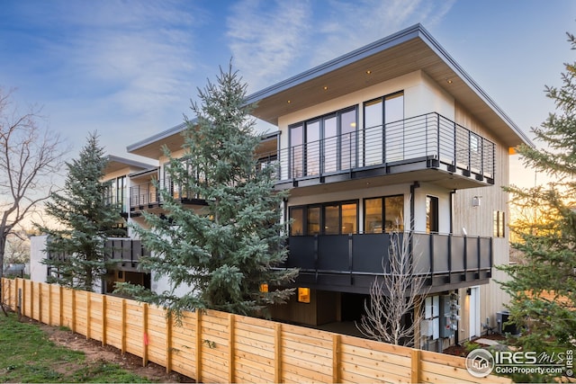 rear view of property featuring a balcony, cooling unit, and a fenced front yard