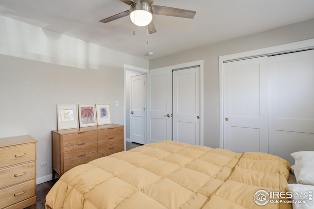 bedroom featuring baseboards, ceiling fan, two closets, and dark wood-style floors