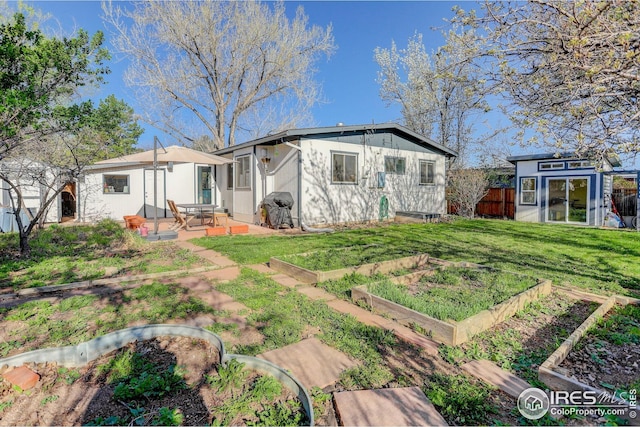 rear view of property featuring a lawn, fence, an outbuilding, and a garden