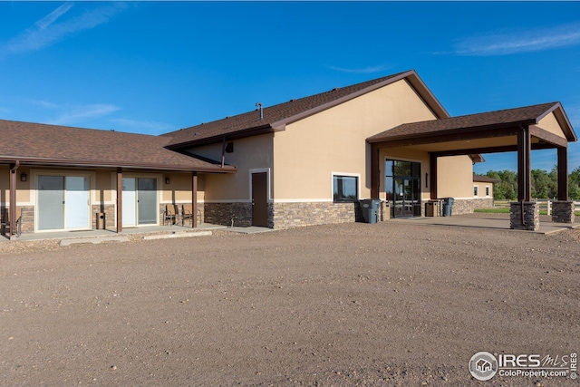 back of house featuring a patio area, stucco siding, and stone siding