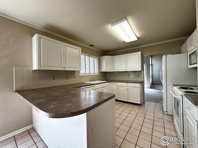 kitchen with a peninsula, a sink, dark countertops, white appliances, and ornamental molding