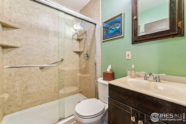 bathroom with a textured wall, vanity, a shower stall, and toilet