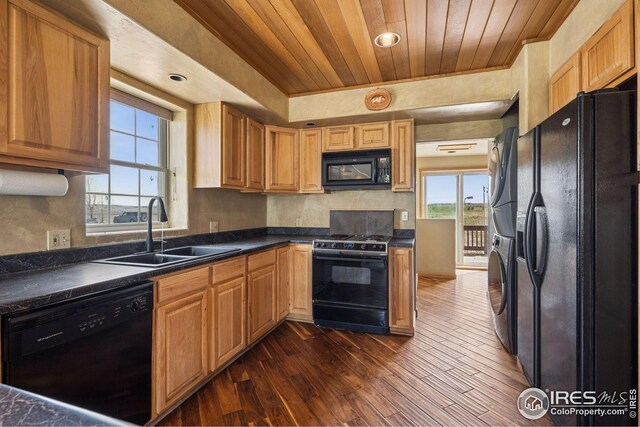 kitchen with wooden ceiling, plenty of natural light, a sink, stacked washer and clothes dryer, and black appliances