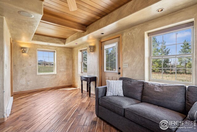 living area with a raised ceiling, wooden ceiling, wood finished floors, and baseboards