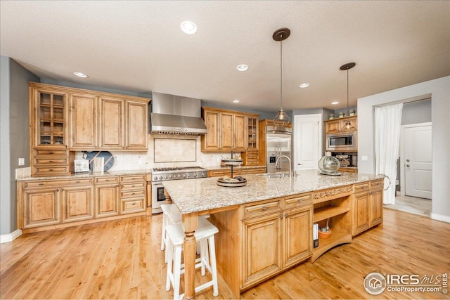 kitchen with wall chimney exhaust hood, light wood-style flooring, open shelves, a sink, and built in appliances