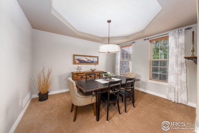 dining room featuring a raised ceiling, light carpet, baseboards, and visible vents